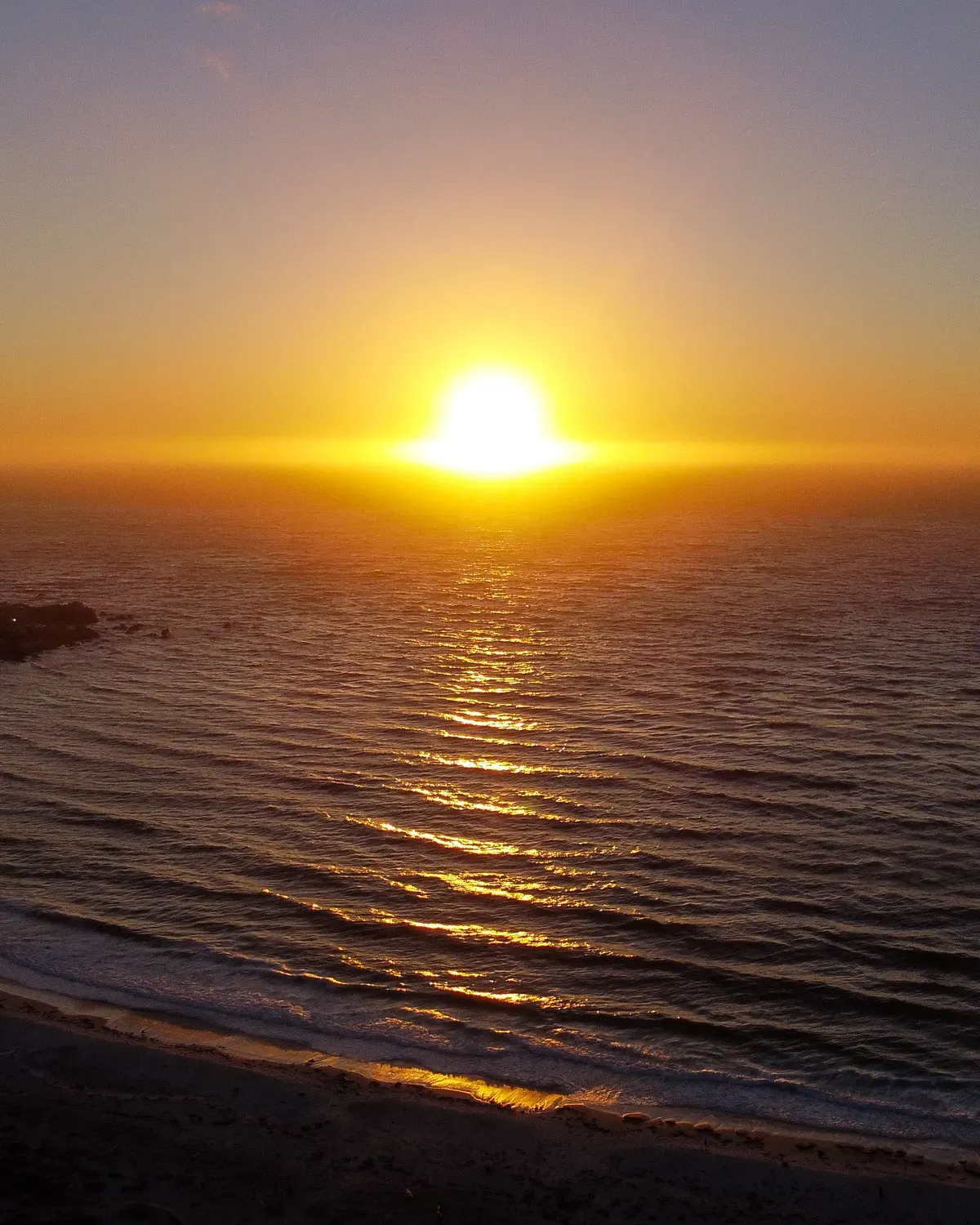 The sun sitting on the horizon over the ocean, its light spread flat across the water