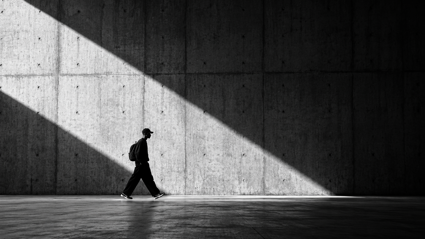A person walking through light and shadow beside a concrete wall